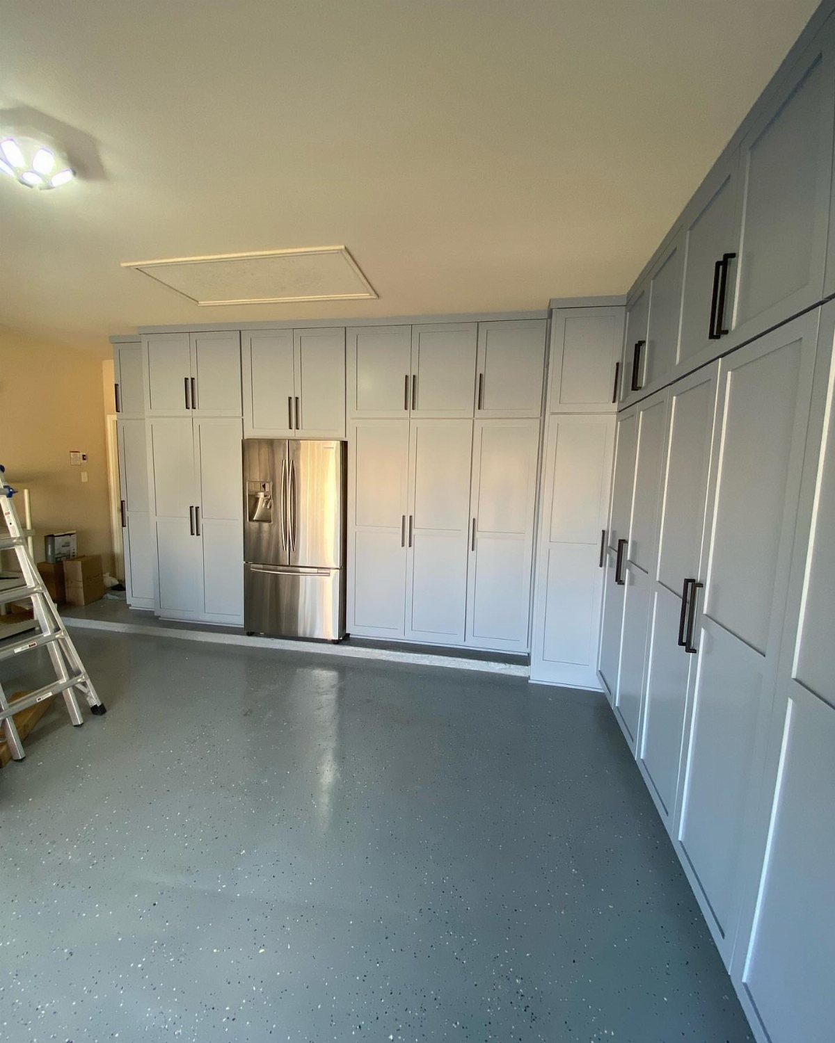 Light blue garage cabinets with dark handles installed on a wall around a stainless steel refrigerator.