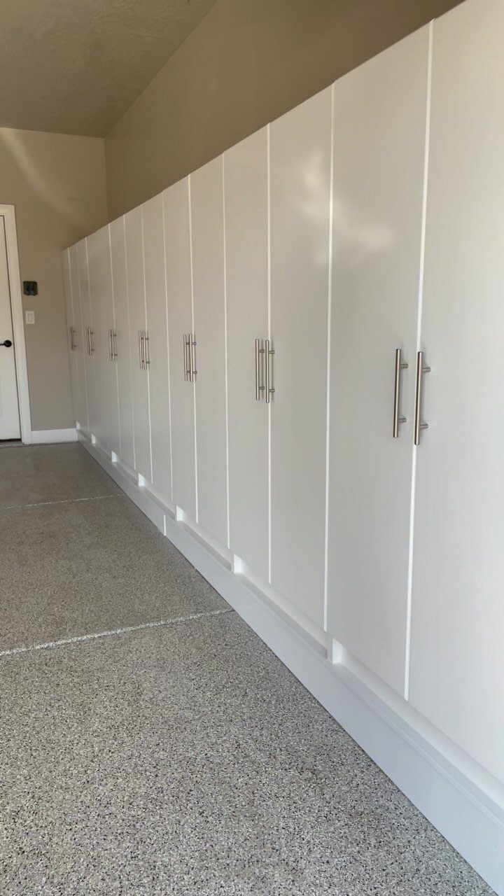 White floor-to-ceiling garage cabinets with silver handles installed along a beige wall and epoxy floor.