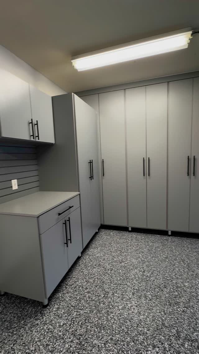 Grey garage storage cabinets and tall wardrobes installed against a wall with black handles.