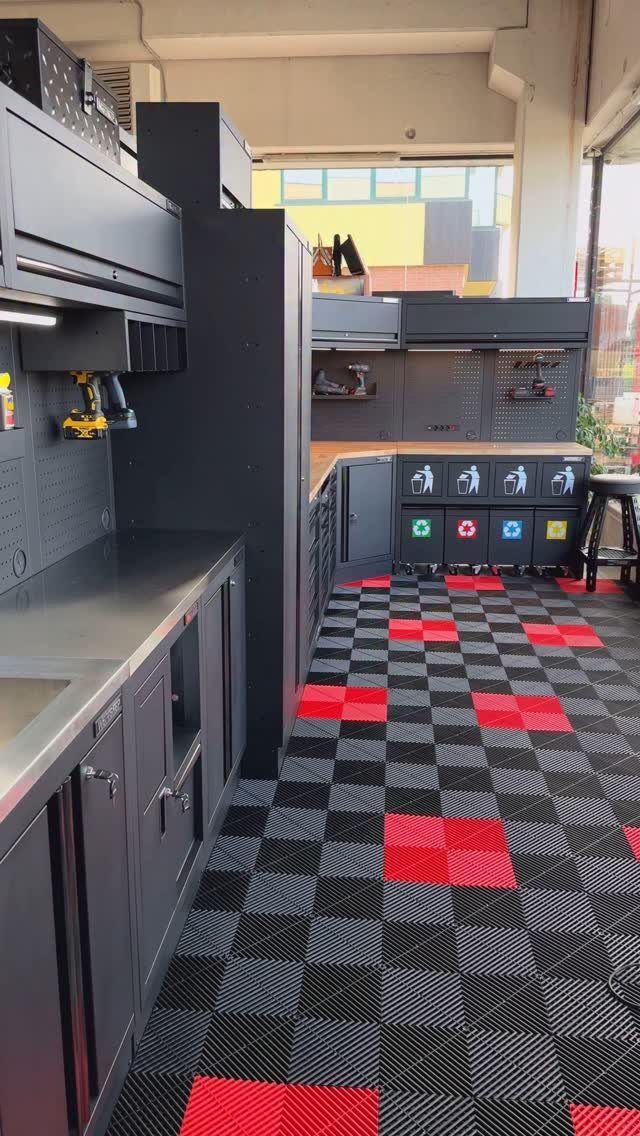 Dark grey garage cabinets and workbenches installed over a black and red checkered floor.