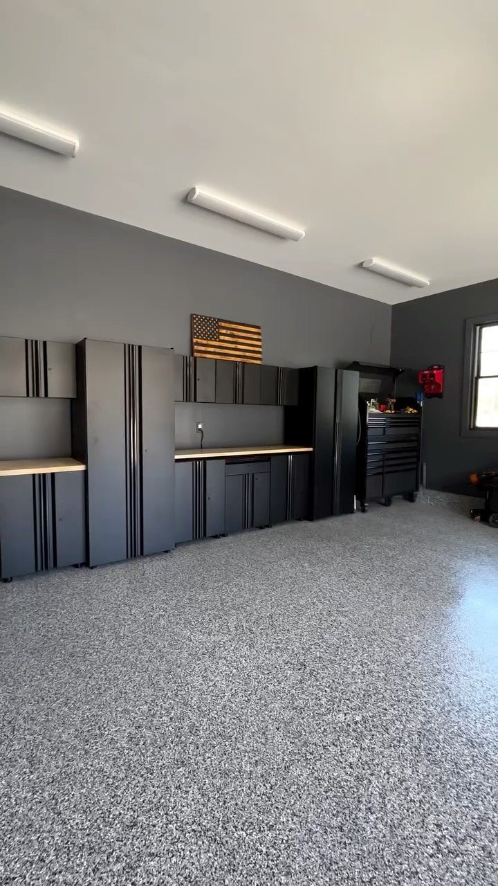 Black garage cabinets and storage units installed against a dark grey wall in a clean garage.