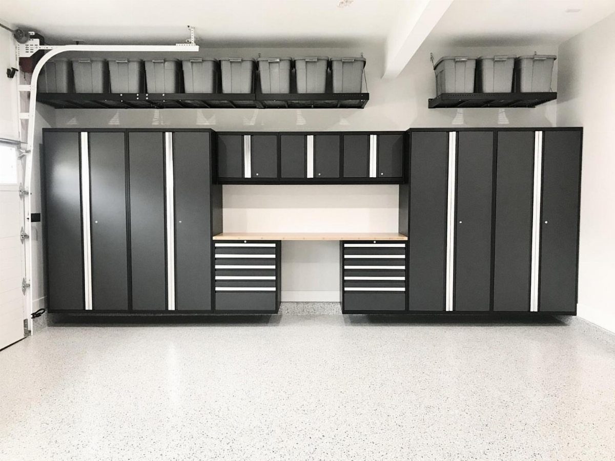 Dark grey garage cabinets with silver accents installed on a white wall above a workbench.