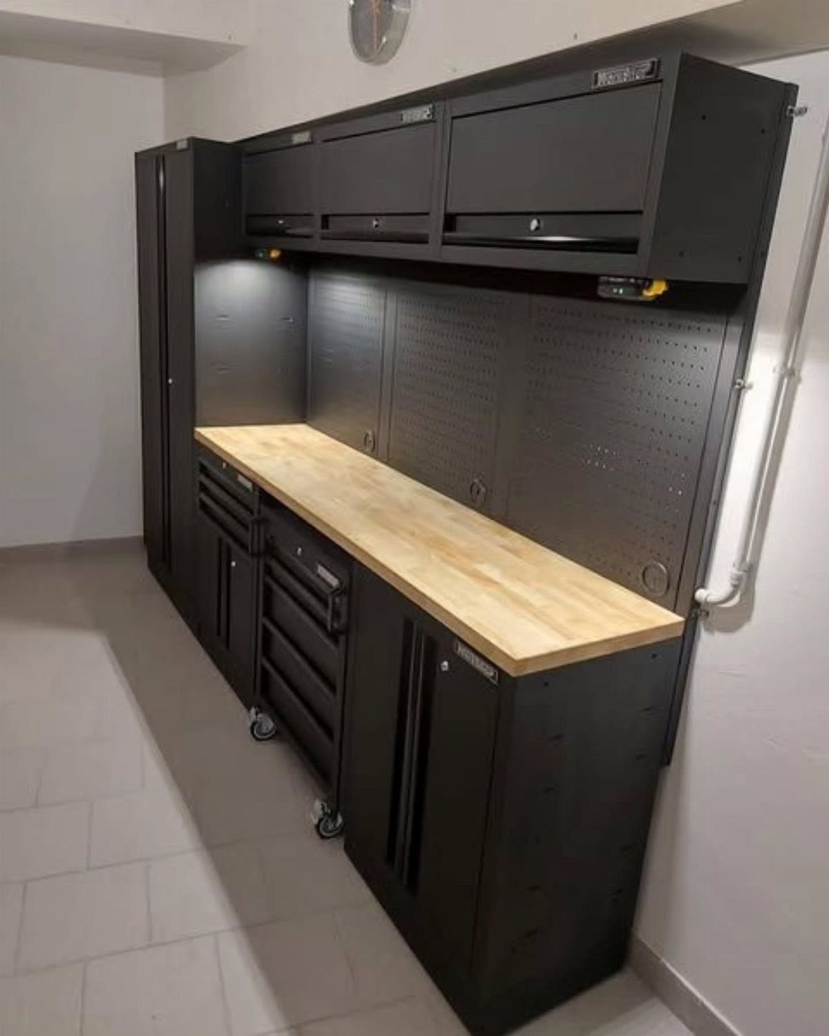 Black garage storage system with a wooden workbench and wall-mounted overhead cabinets.