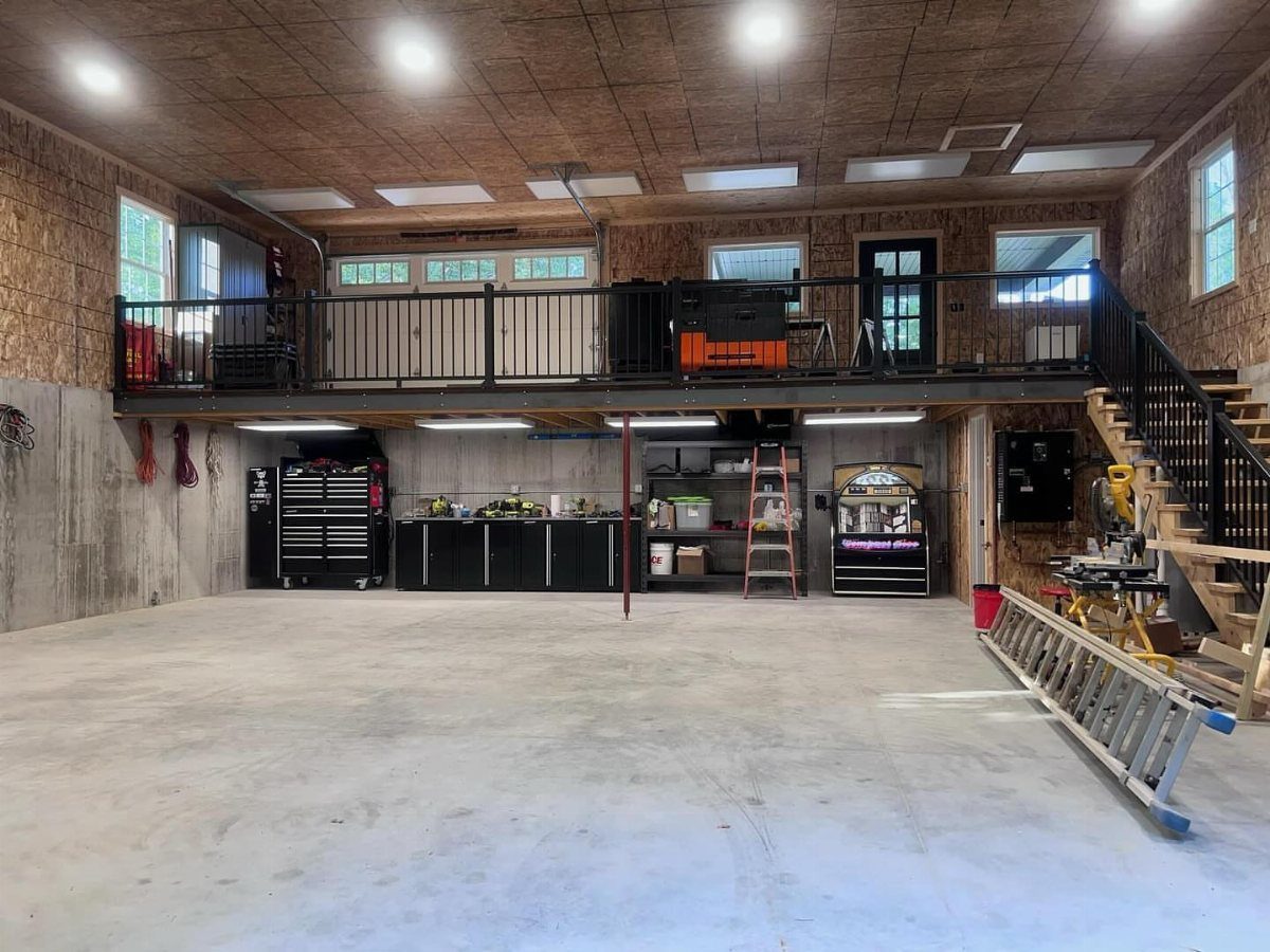 A large wooden storage loft with black railings installed above a garage workshop area.
