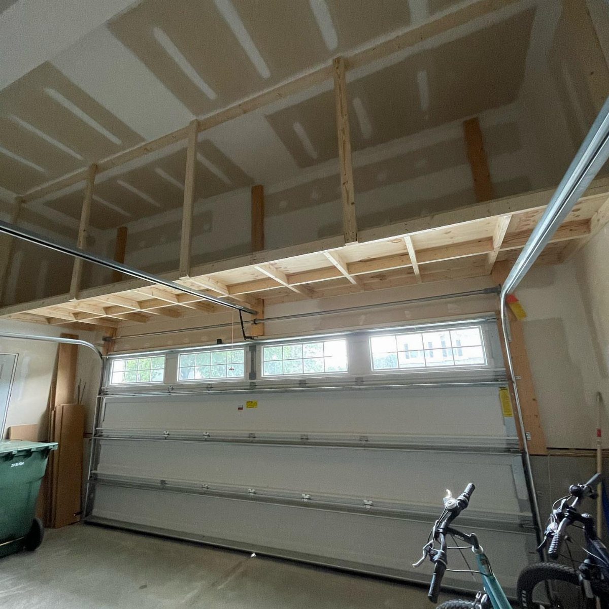 A wooden storage loft constructed with exposed joists above a white garage door.