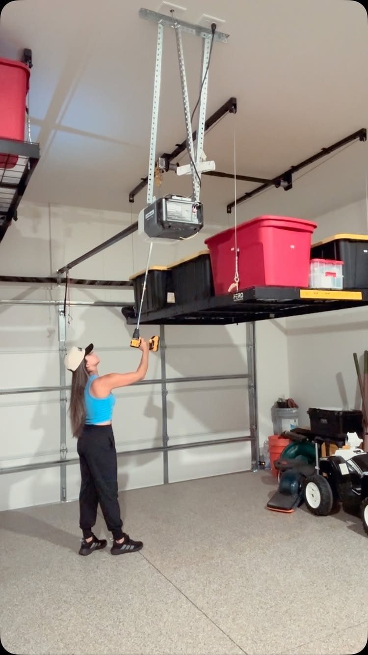 A woman using a drill to install a motorized hoist for garage loft storage.