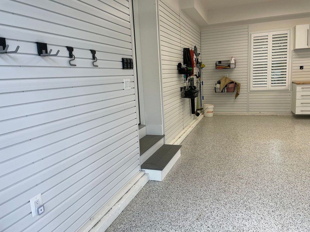 White slatwall panels with black hooks and small shelves installed in a clean garage.