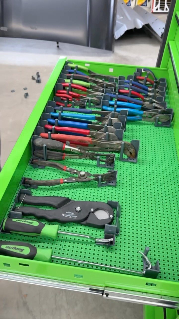Various hand tools organized in black dividers within a bright green tool drawer.