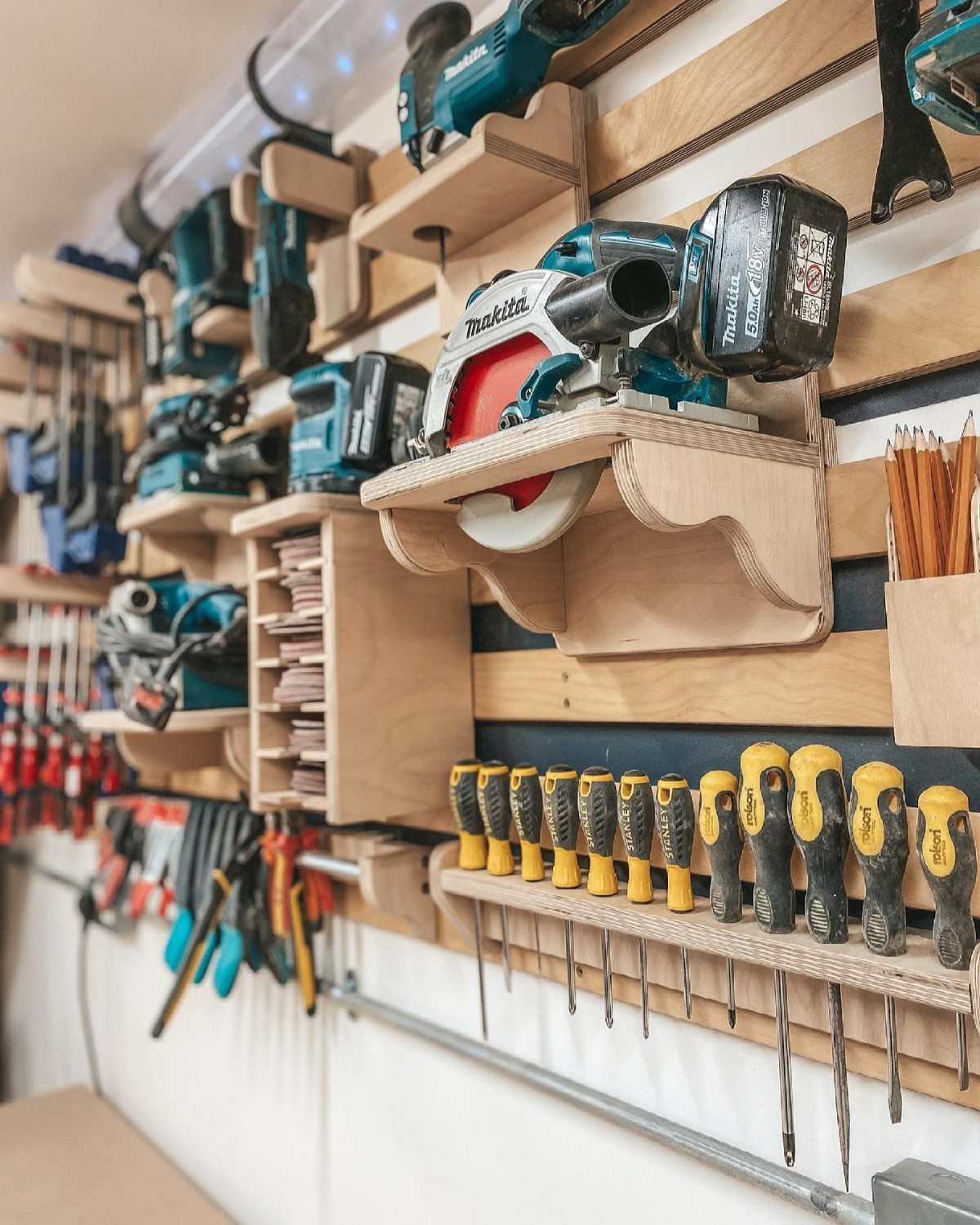 Wooden slatwall system holding power tools and screwdrivers in a garage workshop setting.