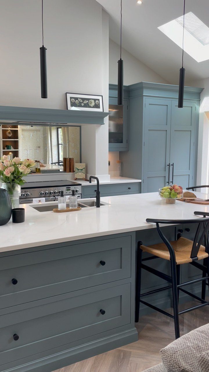 Blue-grey kitchen cabinets and white marble countertops with black pendant lights and a large island.