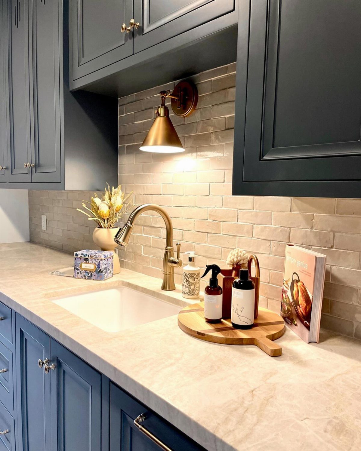 Blue kitchen cabinets set against a light grey subway tile backsplash with a gold faucet.