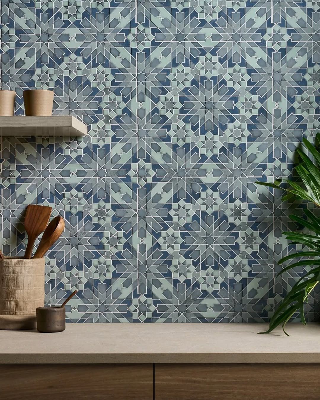 Patterned blue and grey geometric tiles covering a kitchen backsplash wall near wooden utensils.