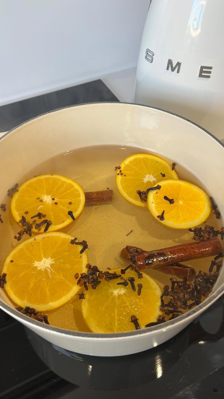 Orange slices, cinnamon sticks, and cloves simmering in a white pot of water on a stove.