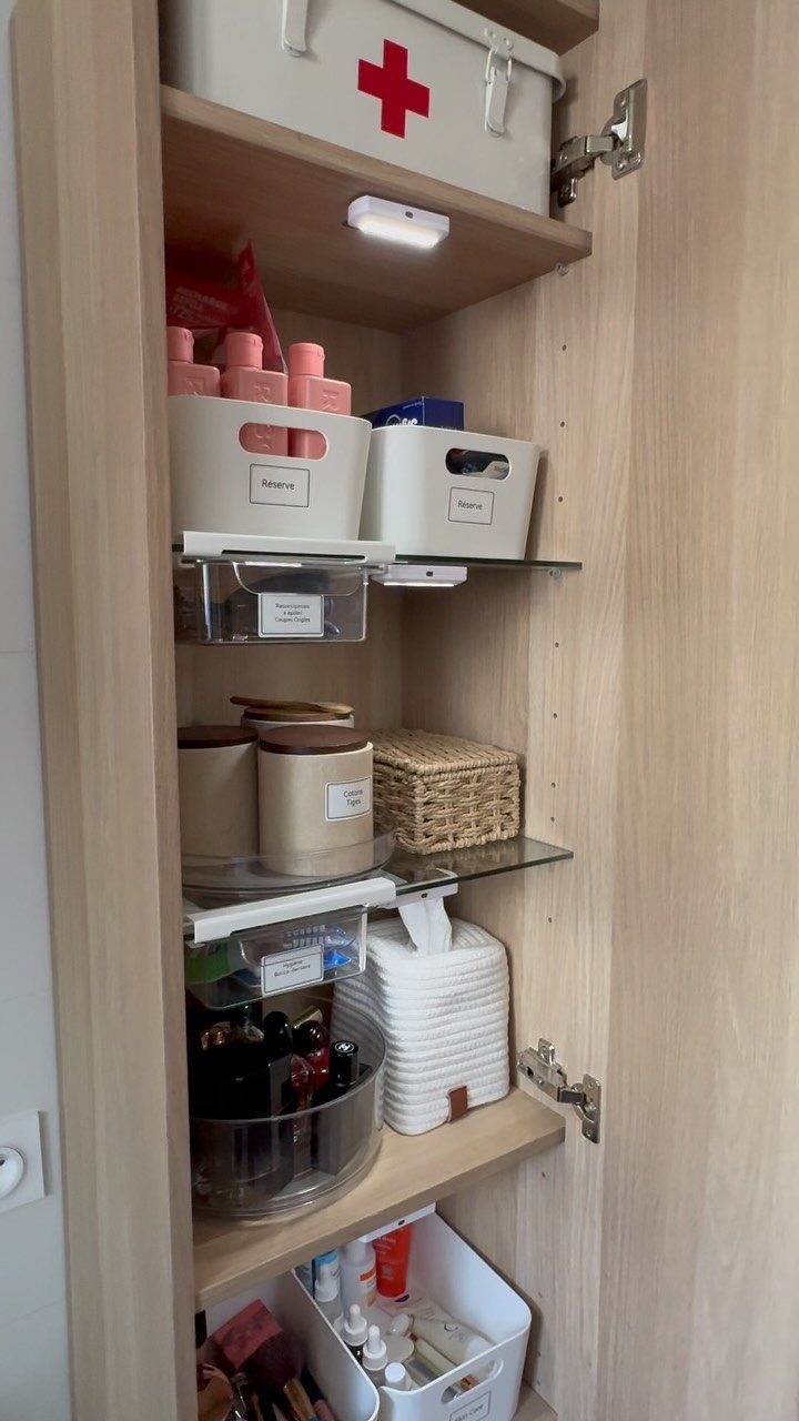 An open wooden cabinet filled with organized white bins, clear containers, and various storage baskets.
