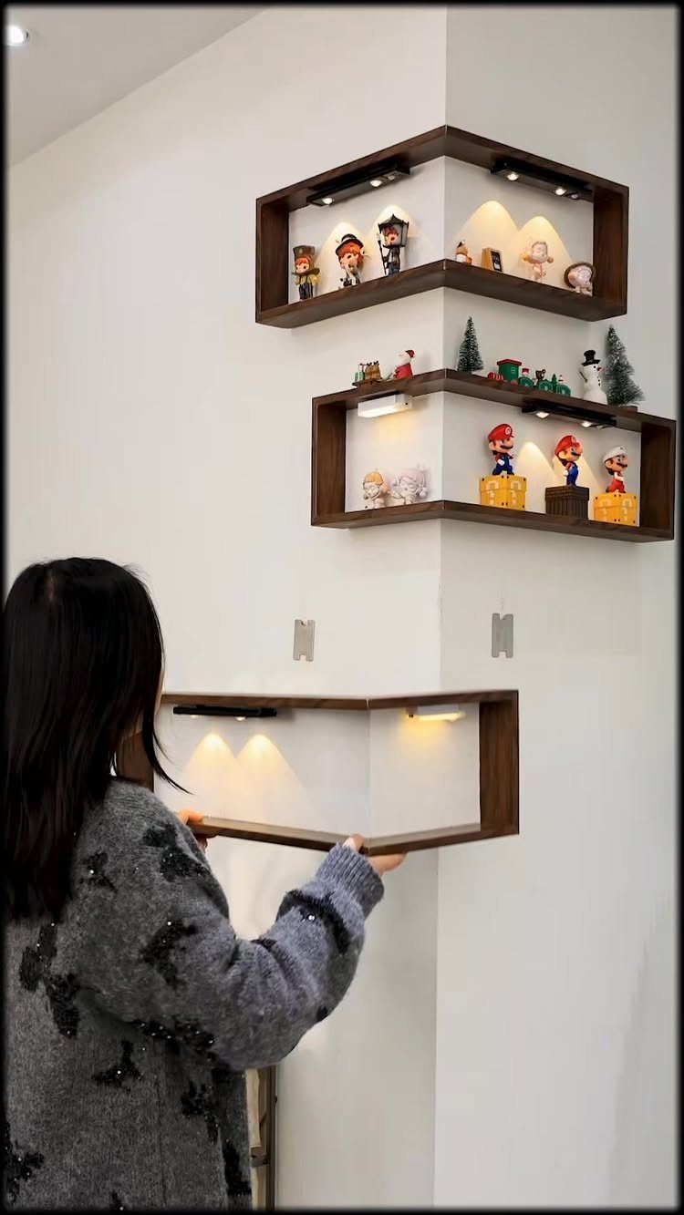A person installing illuminated dark wood corner shelves on a white wall for decorative storage.