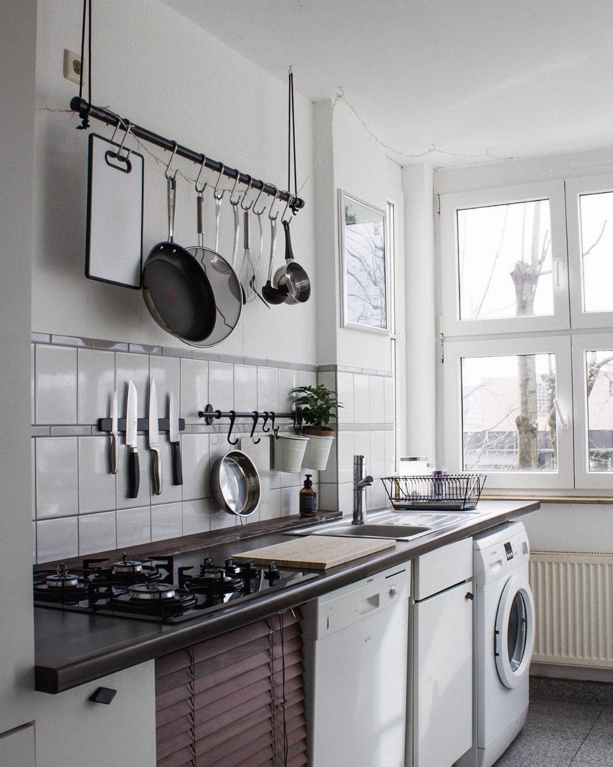 Kitchen utensils and pans hanging from a ceiling rack and magnetic strip above a countertop.