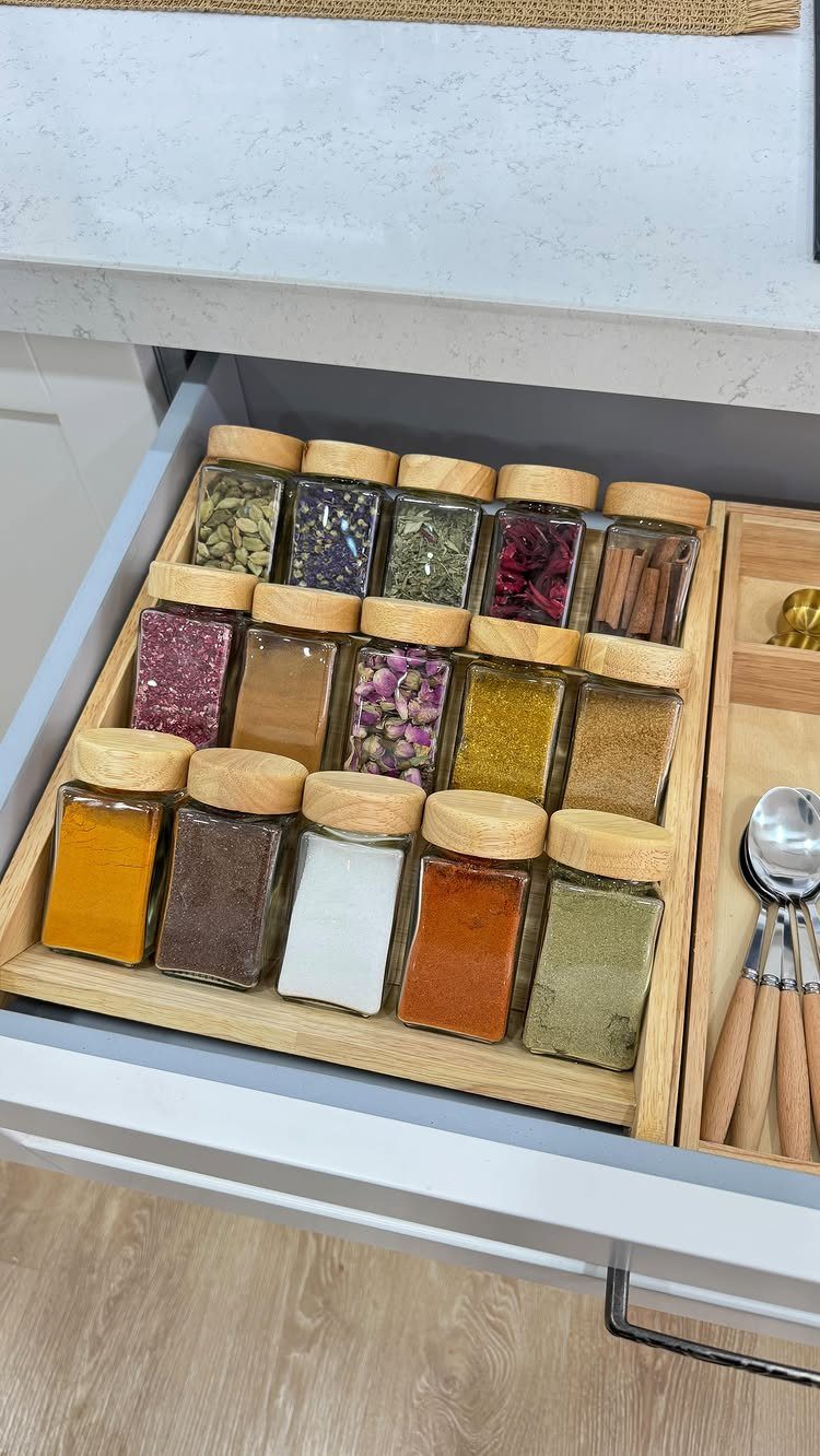 Small glass spice jars with wooden lids organized in a bamboo rack inside a kitchen drawer.
