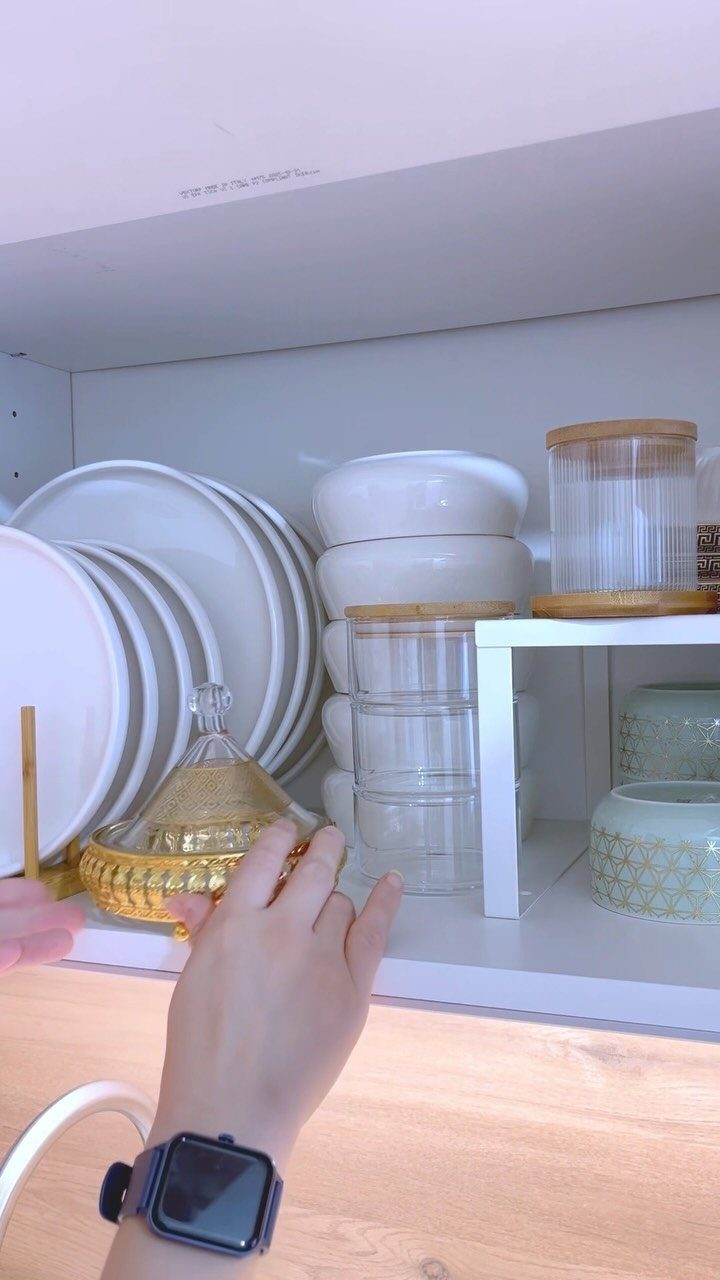 White plates and glass canisters organized neatly on white kitchen cabinet shelves.