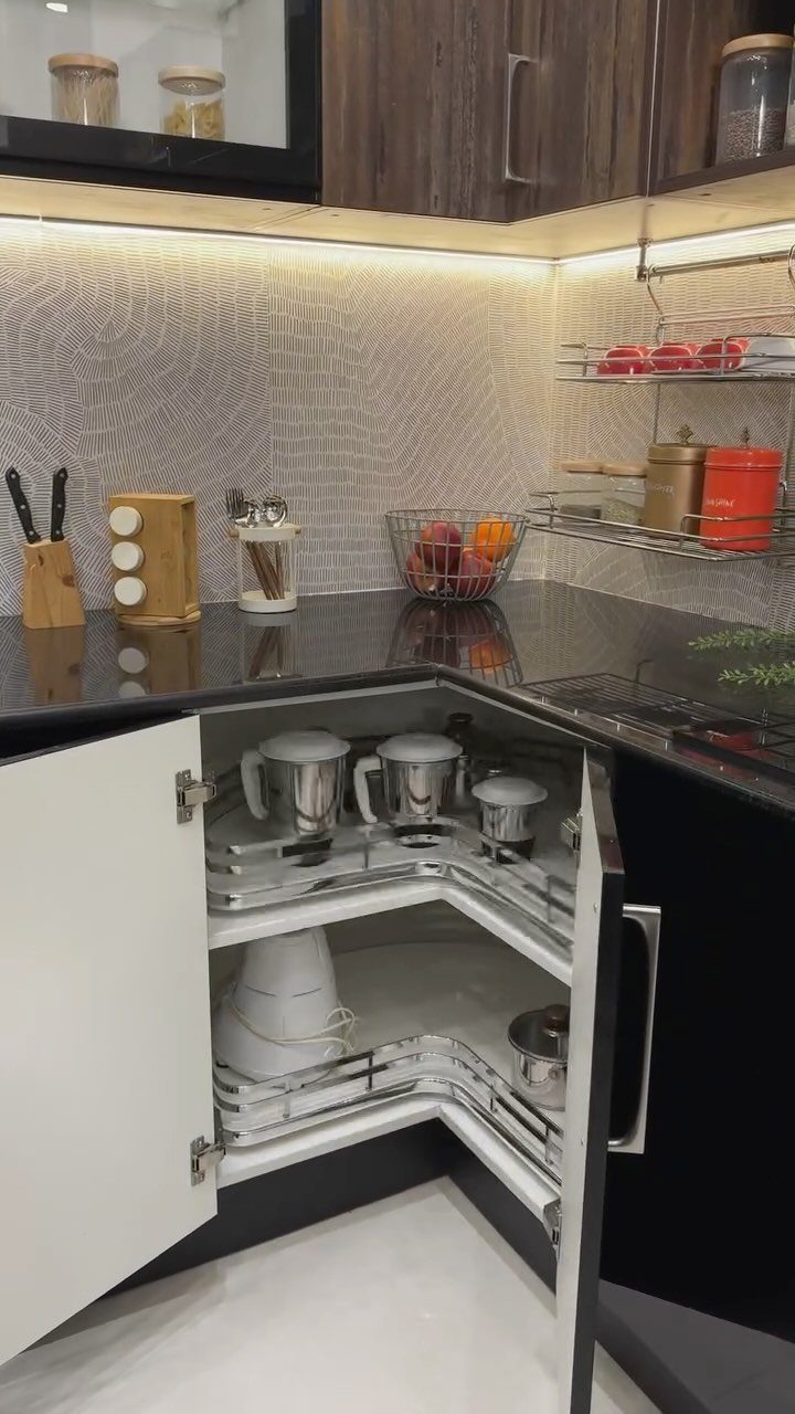 White pull-out shelves inside an open corner kitchen cabinet holding various stainless steel kitchen appliances.