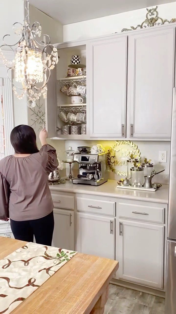 A woman opens a white kitchen cabinet filled with neatly arranged patterned mugs and teacups.