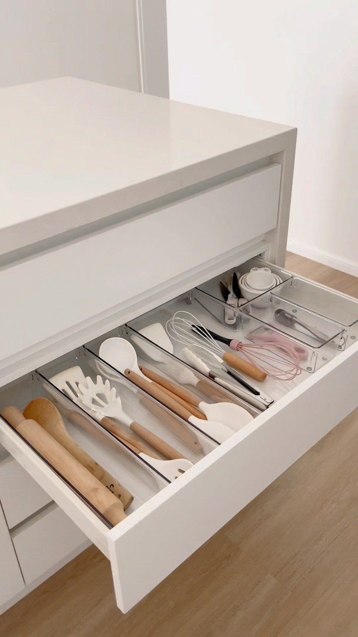 White kitchen drawer organized with clear dividers holding wooden and silicone cooking utensils.