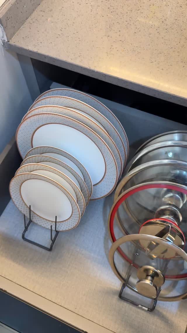 Patterned plates in a wire rack and stainless steel pots inside a kitchen cabinet.