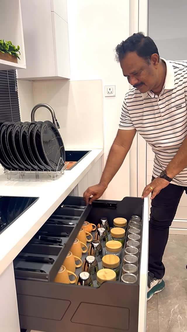 A man organizing small glass jars and containers inside a modern kitchen drawer system.
