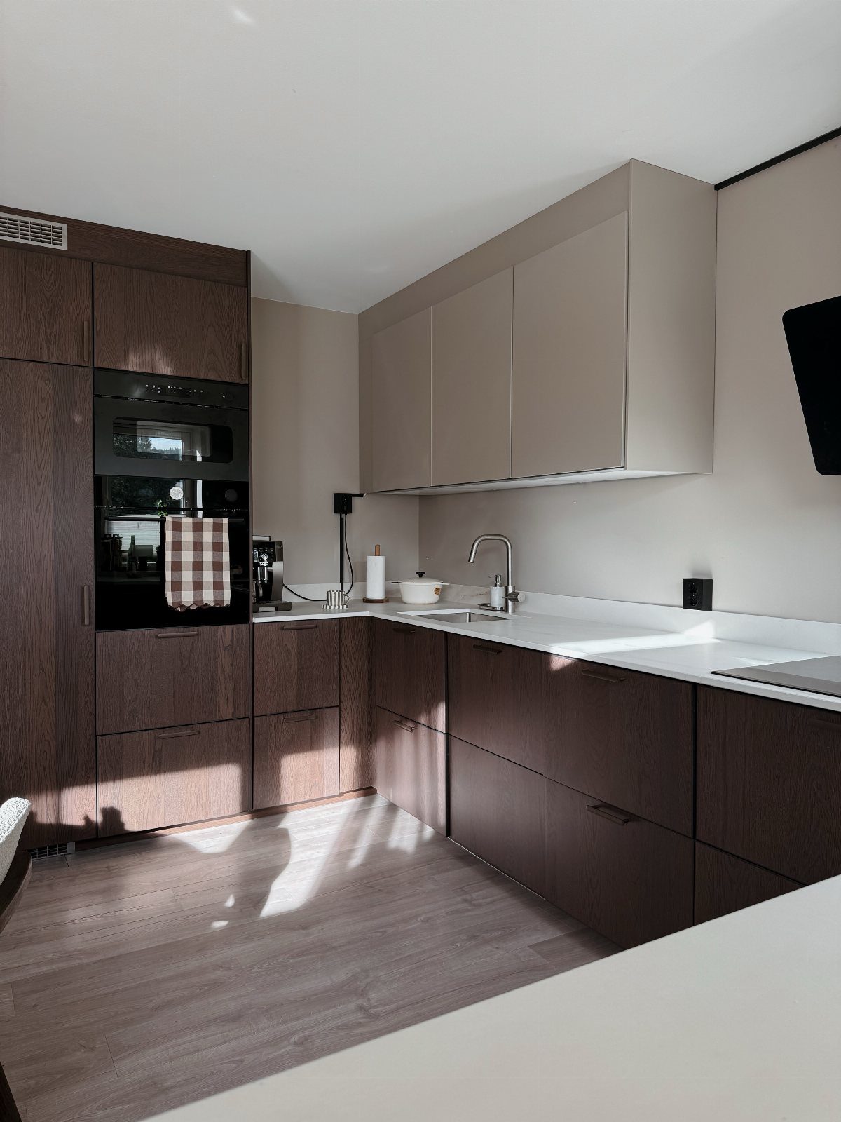 Modern L-shaped kitchen with dark wood lower cabinets and light beige upper cabinets.