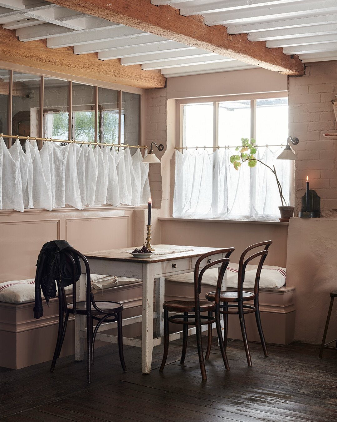 A rustic dining set with a built-in bench, white table, and wooden chairs in a farmhouse kitchen.
