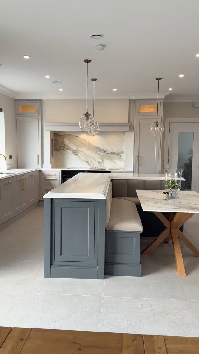 Built-in grey kitchen bench seating integrated into a white marble island next to a wooden table.