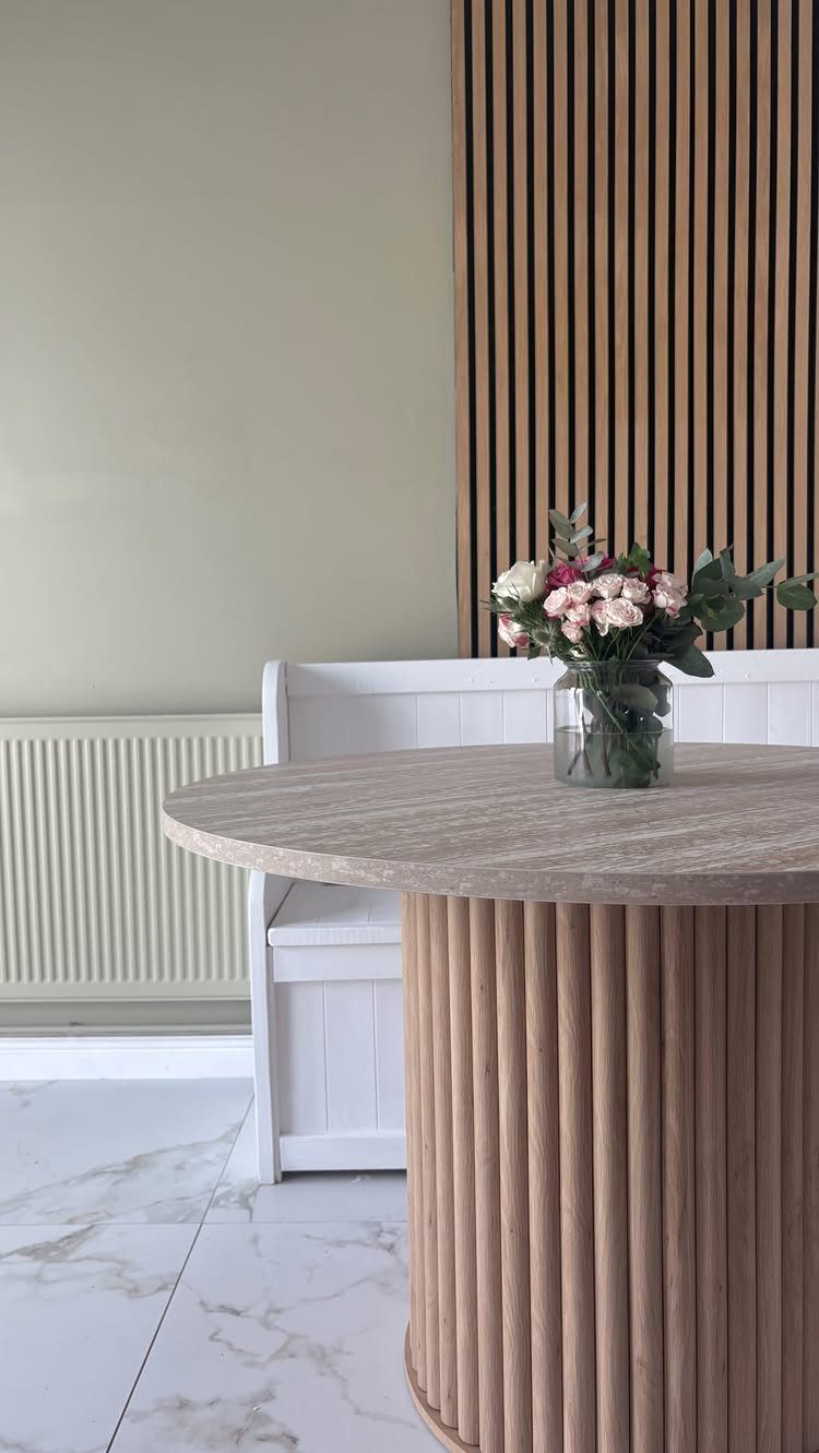 White wooden banquette seating next to a round wooden table with flowers in a vase.