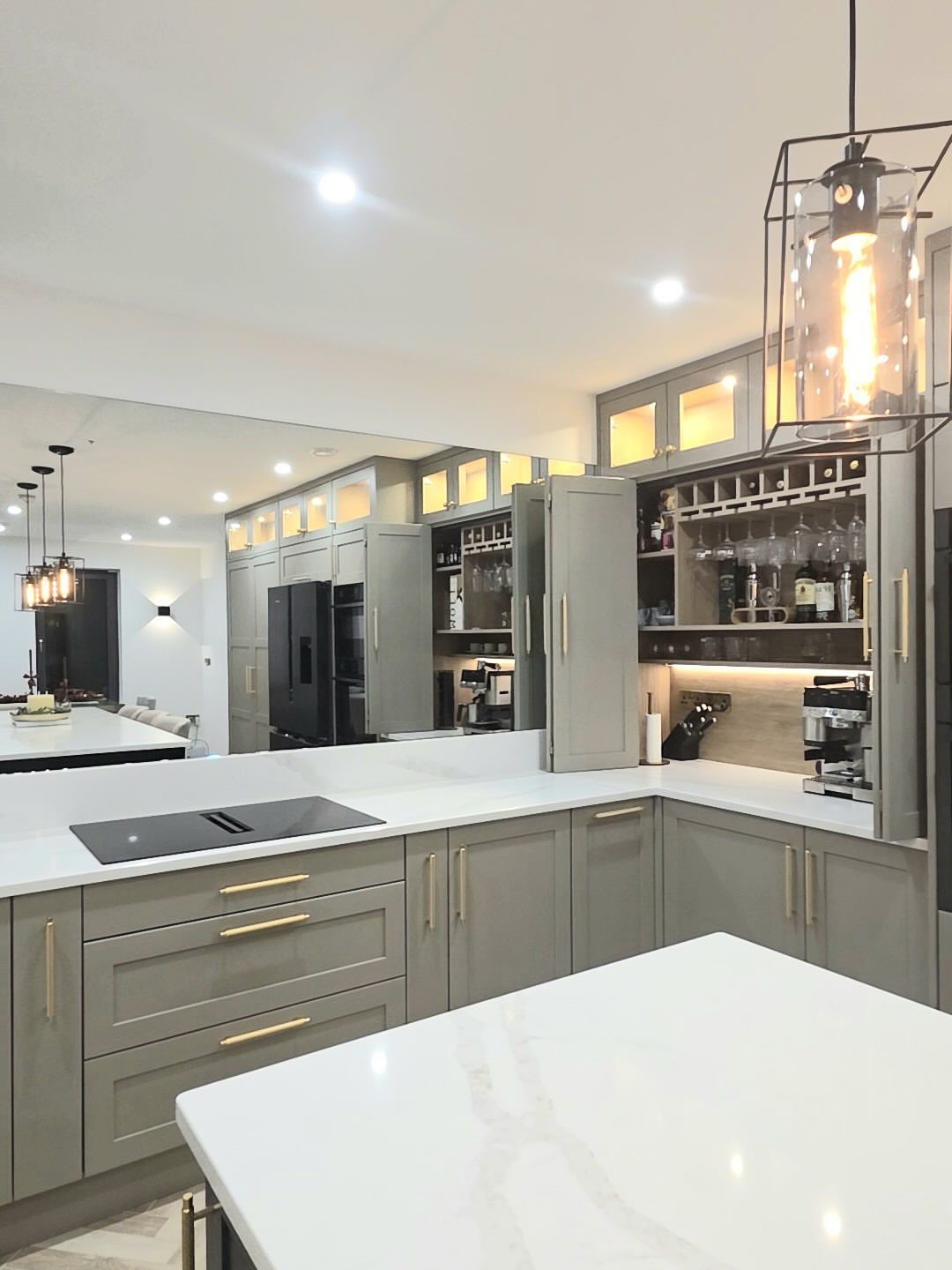 Gray kitchen cabinets with gold hardware and white marble countertops under warm lighting.