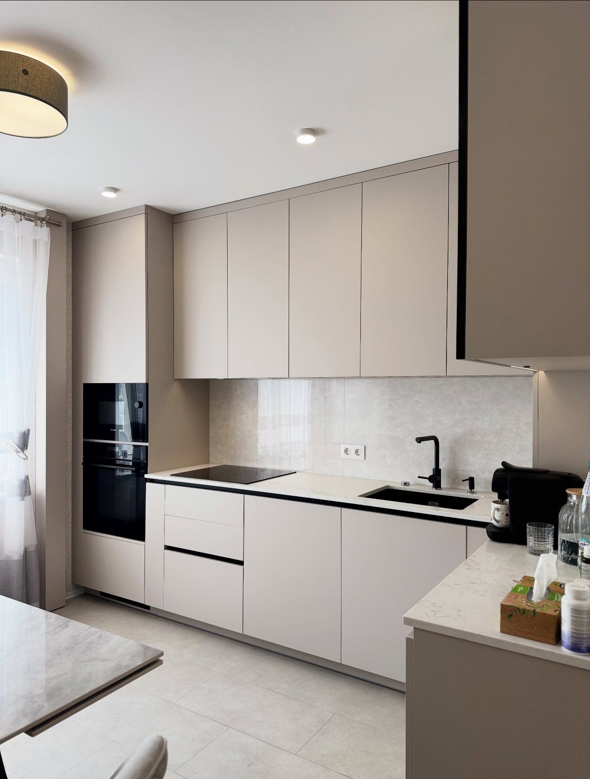 Modern kitchen with minimalist greige cabinets, white countertops, and a black sink and faucet.