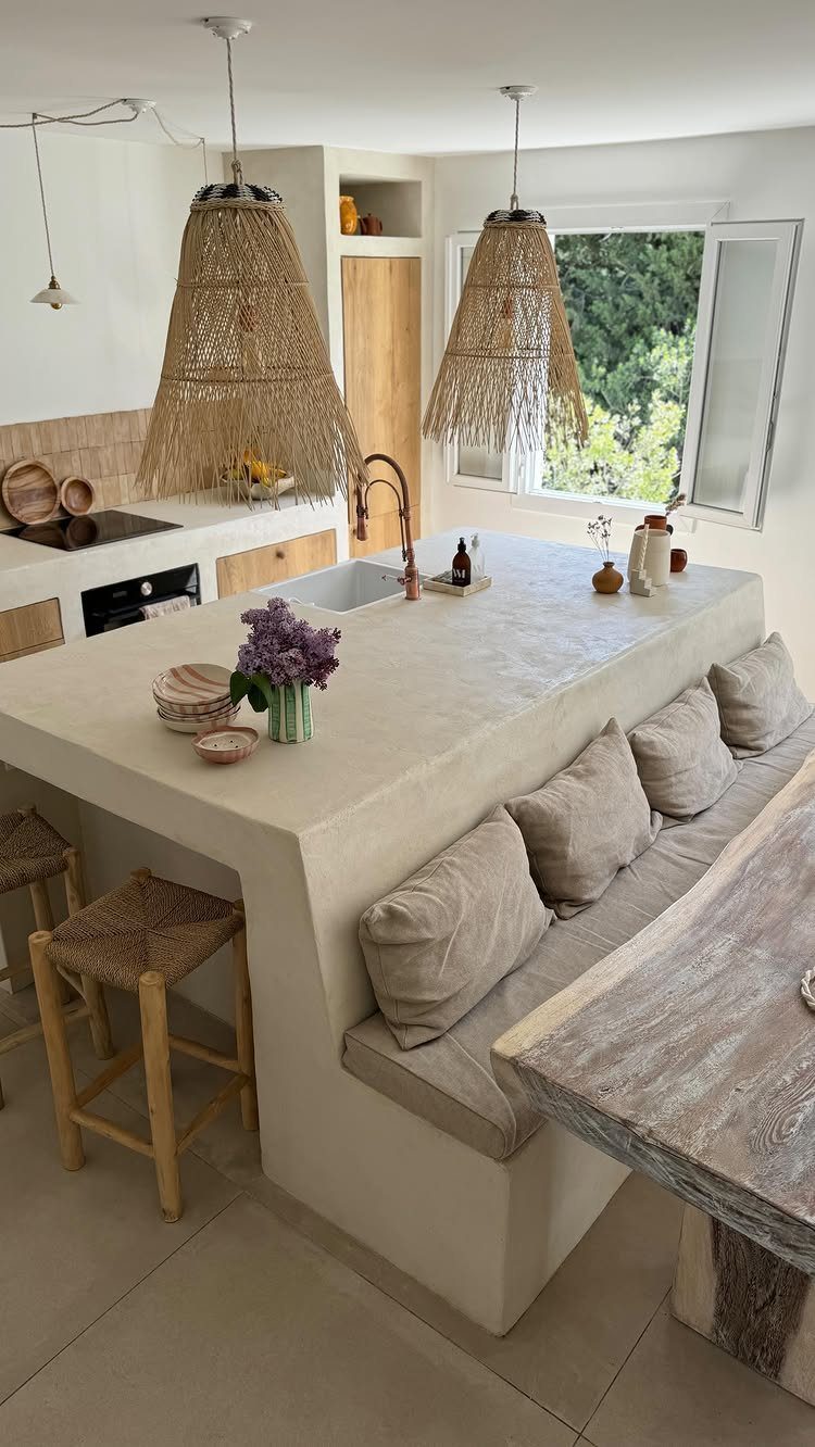 A bright kitchen island with built-in seating and woven pendant lights overlooking a window.