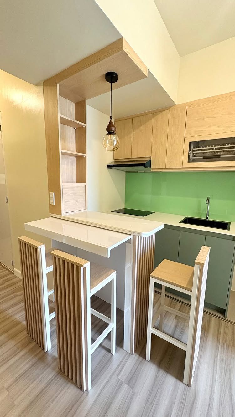 Modern kitchen with light wood cabinets, green backsplash, and a white breakfast bar with wooden stools.