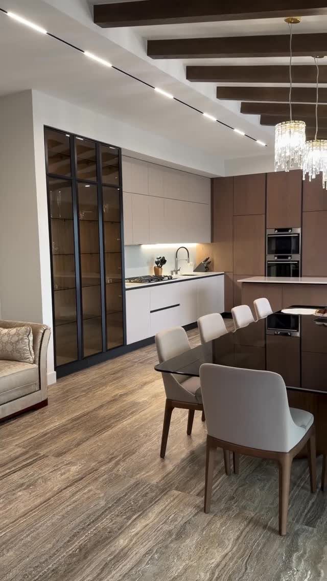 Modern open-plan living space with a dining table, kitchen cabinets, and wood-beamed ceiling.