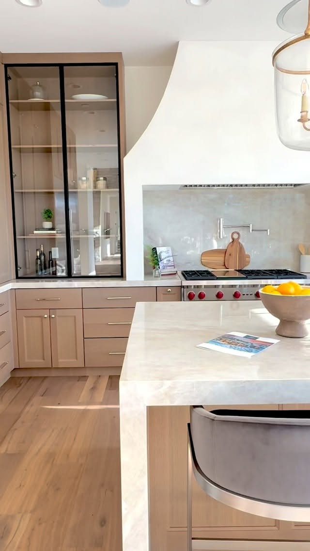 Modern kitchen with light wood cabinets, marble countertops, and a large island with a bowl of lemons.