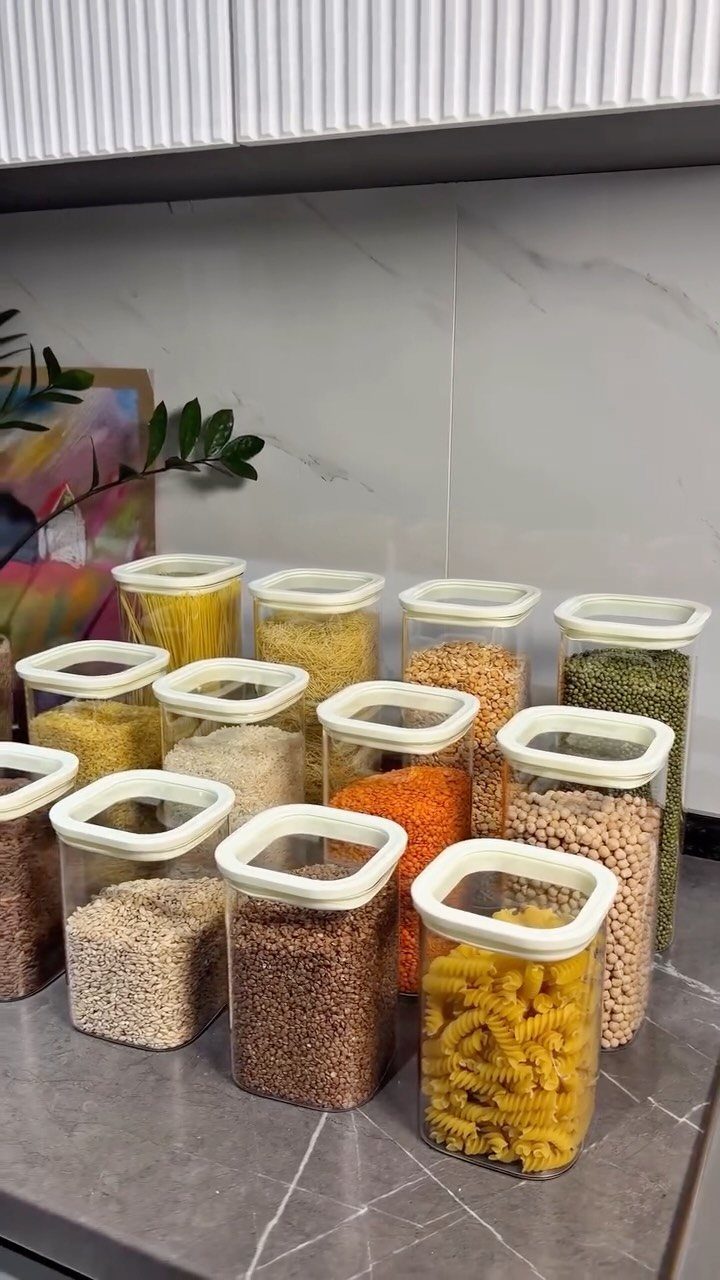 Clear plastic containers with white lids filled with various dry goods on a marble countertop.