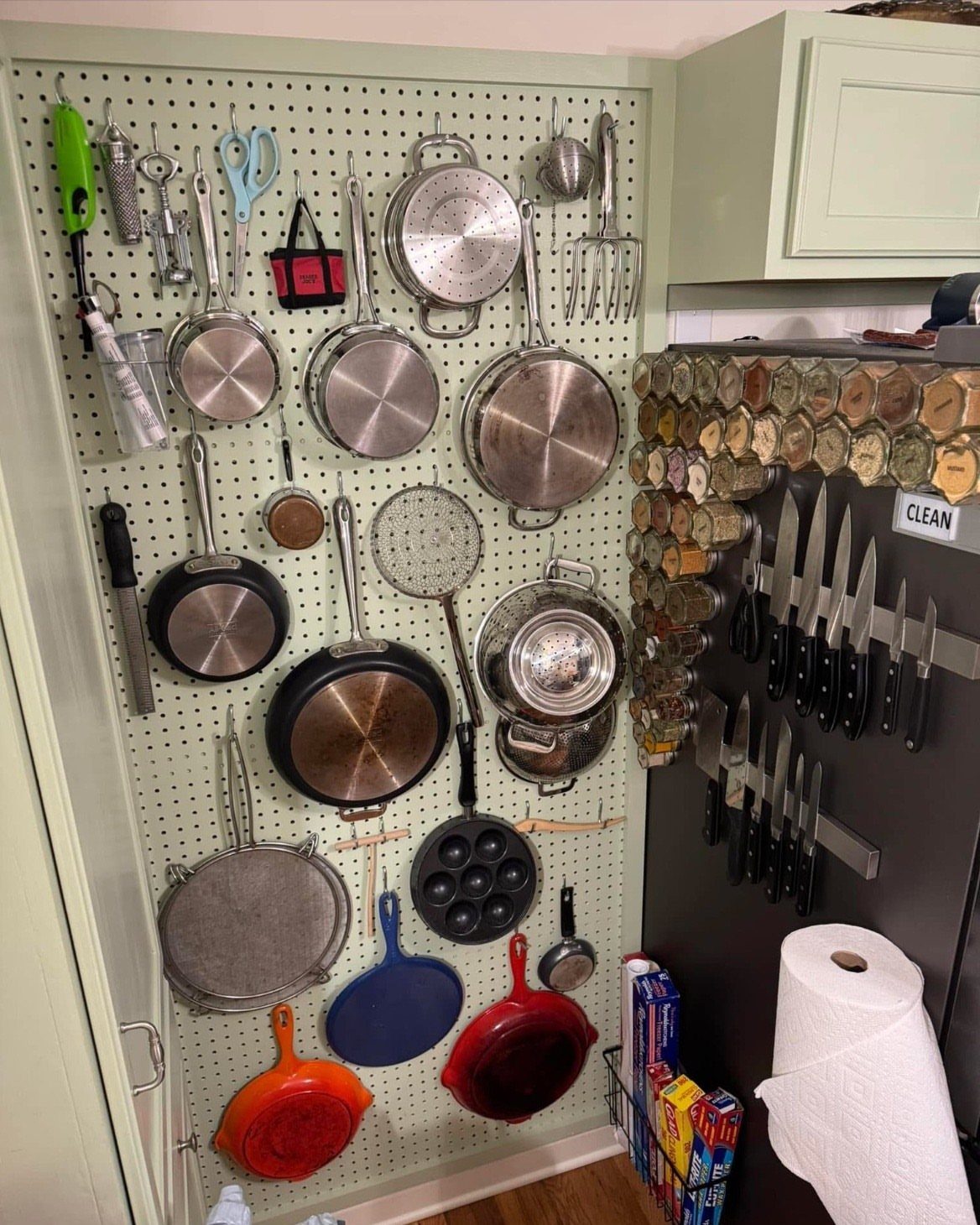 Various kitchen pans and utensils hanging organized on a large white pegboard wall.