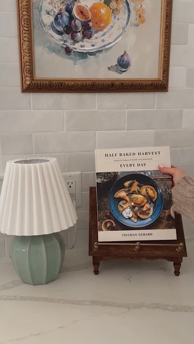 A hand placing a cookbook onto a small wooden stand on a marble countertop.
