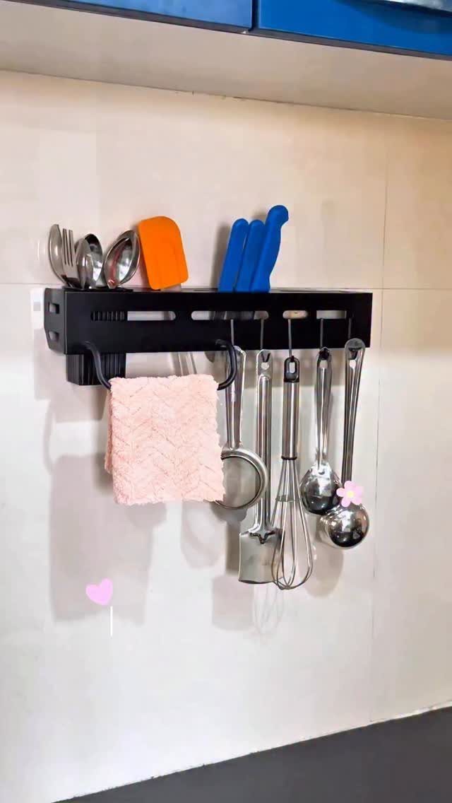 Black wall-mounted kitchen utensil organizer holding various metal and plastic cooking tools against a white wall.