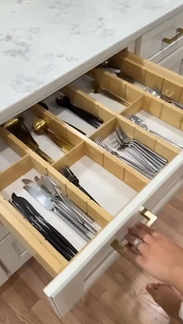 Silverware organized in light wood drawer dividers within an open white kitchen drawer.