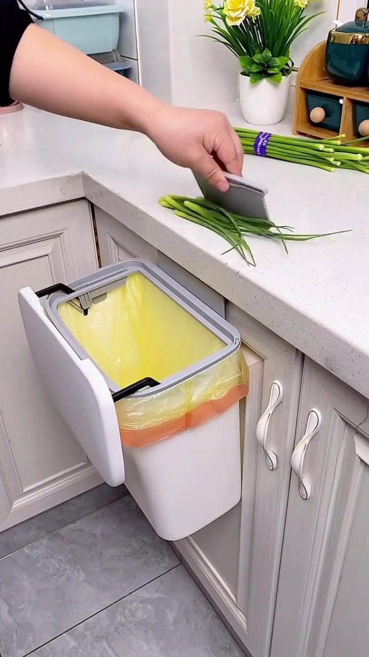 A person chops green onions on a white counter next to a mounted kitchen trash bin.