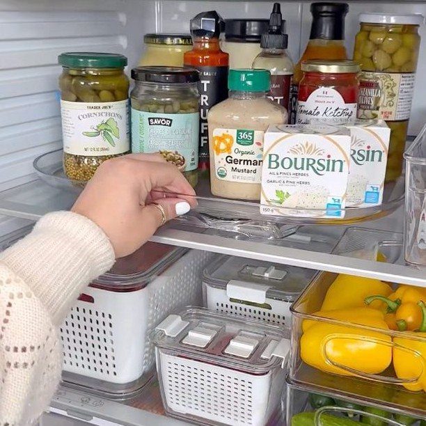 A hand reaches for a clear condiment organizer tray inside a well-organized refrigerator.