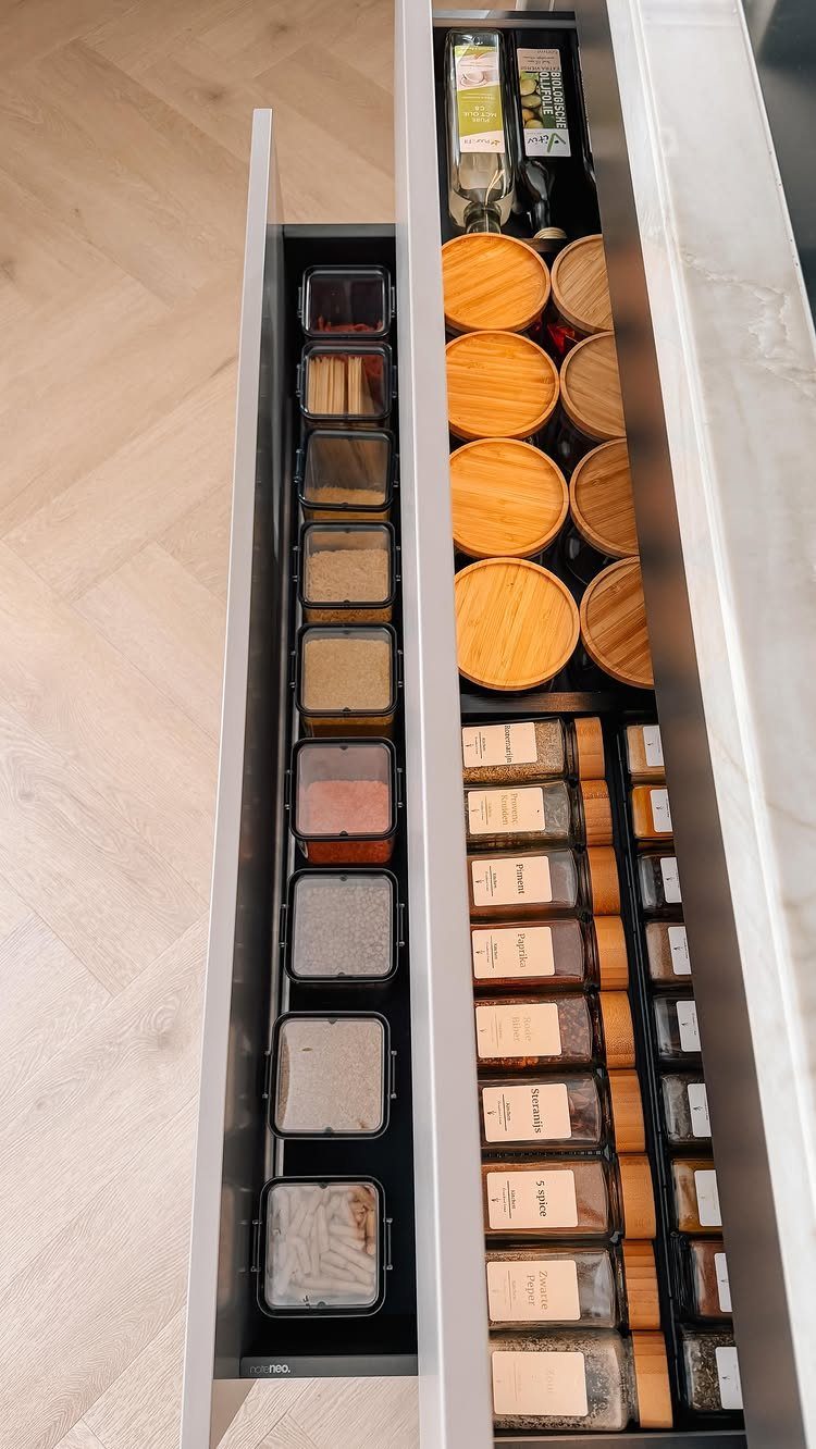 Open kitchen drawers filled with organized spice jars and wooden-lidded containers on a light wood floor.