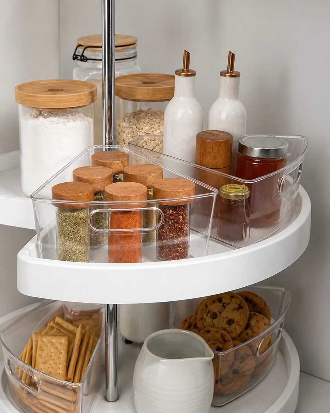 A white two-tier rotating lazy Susan organizer holding various glass jars and food containers.