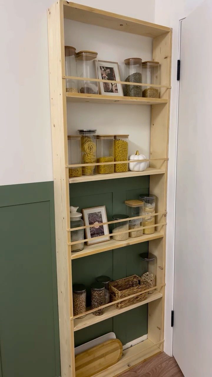 A tall wooden open shelving unit filled with glass jars and small baskets against a wall.