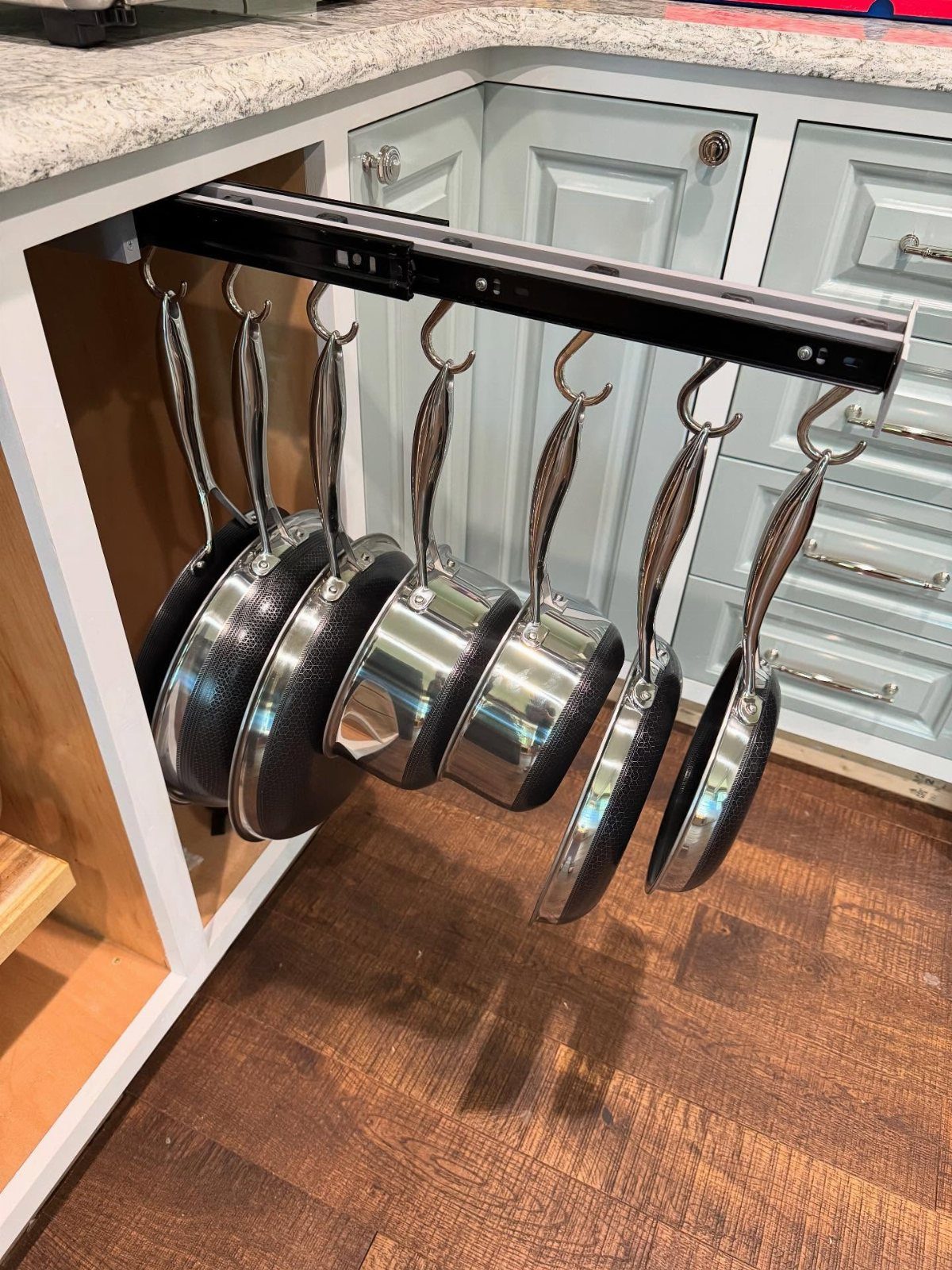 Silver pans hanging from a black pull-out organizer inside an open kitchen cabinet.