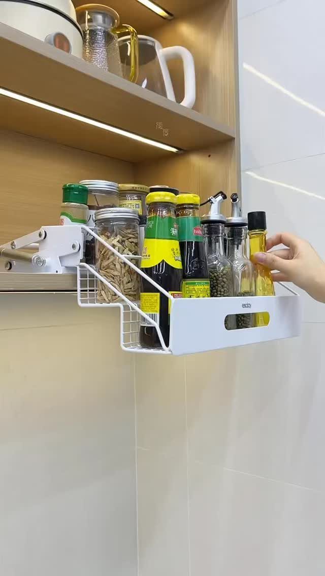A white pull-out organizer tray holding various spice and sauce bottles under a wooden kitchen cabinet.