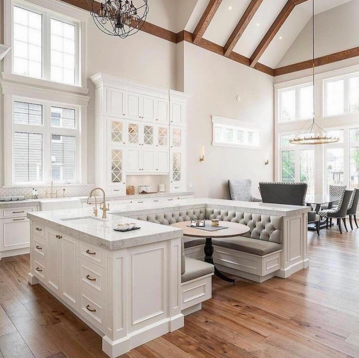 Spacious white kitchen with marble island, built-in banquette seating, and vaulted ceilings with wooden beams.